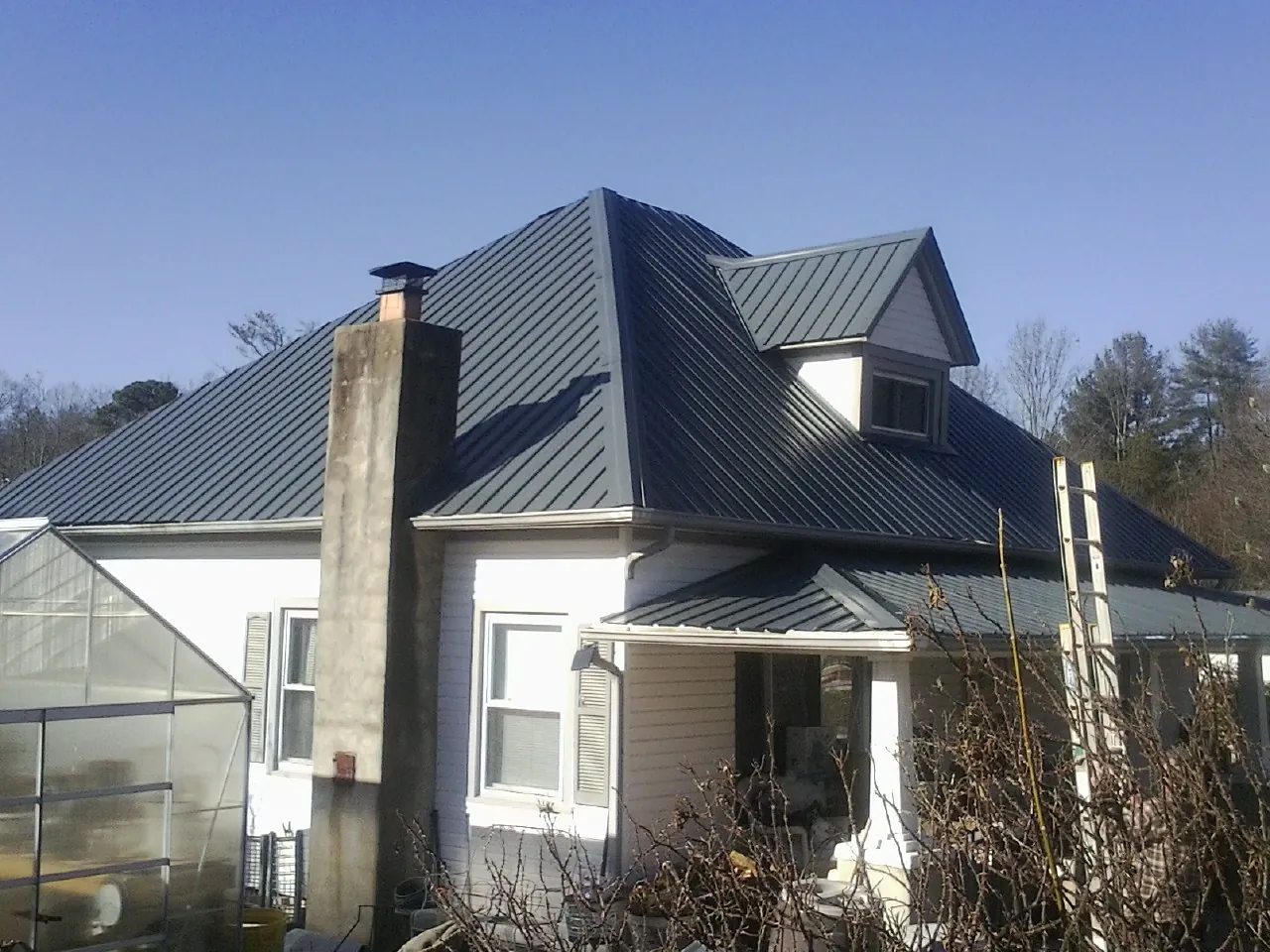 Dark blue standing seam metal roof on a white farmhouse with dormer — Slate & Tile Roof Repair by Roofing Brothers in Rawlings