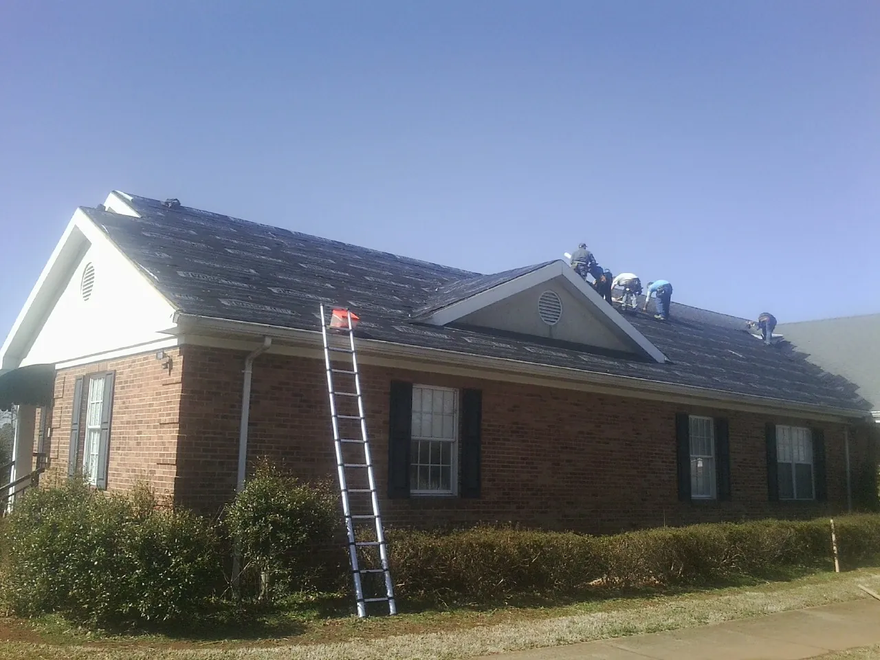 Crew tearing shingles off a brick ranch roof with a ladder set — Emergency Roof Repair work by our crew in Rawlings