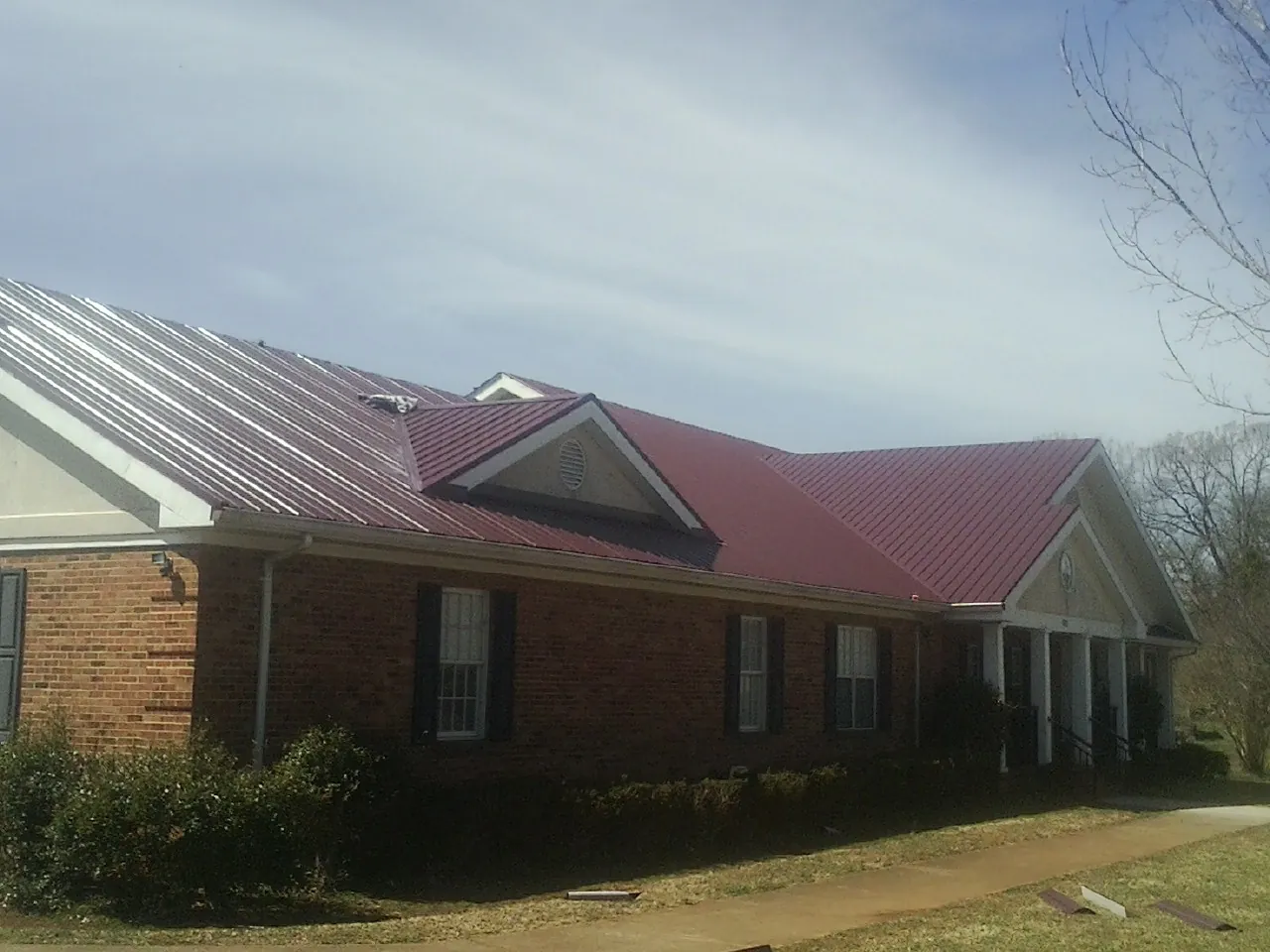 Red metal roof with gabled entries on a long brick building, from a Hail Damage Roof Repair job in Rawlings