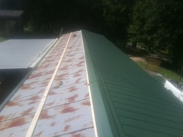 Old rusted panels beside newly installed green metal roofing — Wind Damage Roof Repair by Roofing Brothers in Rawlings
