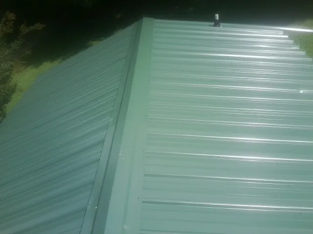 New green metal panels meeting at the ridge of a roof — Flat Roof Repair work by our crew in Rawlings