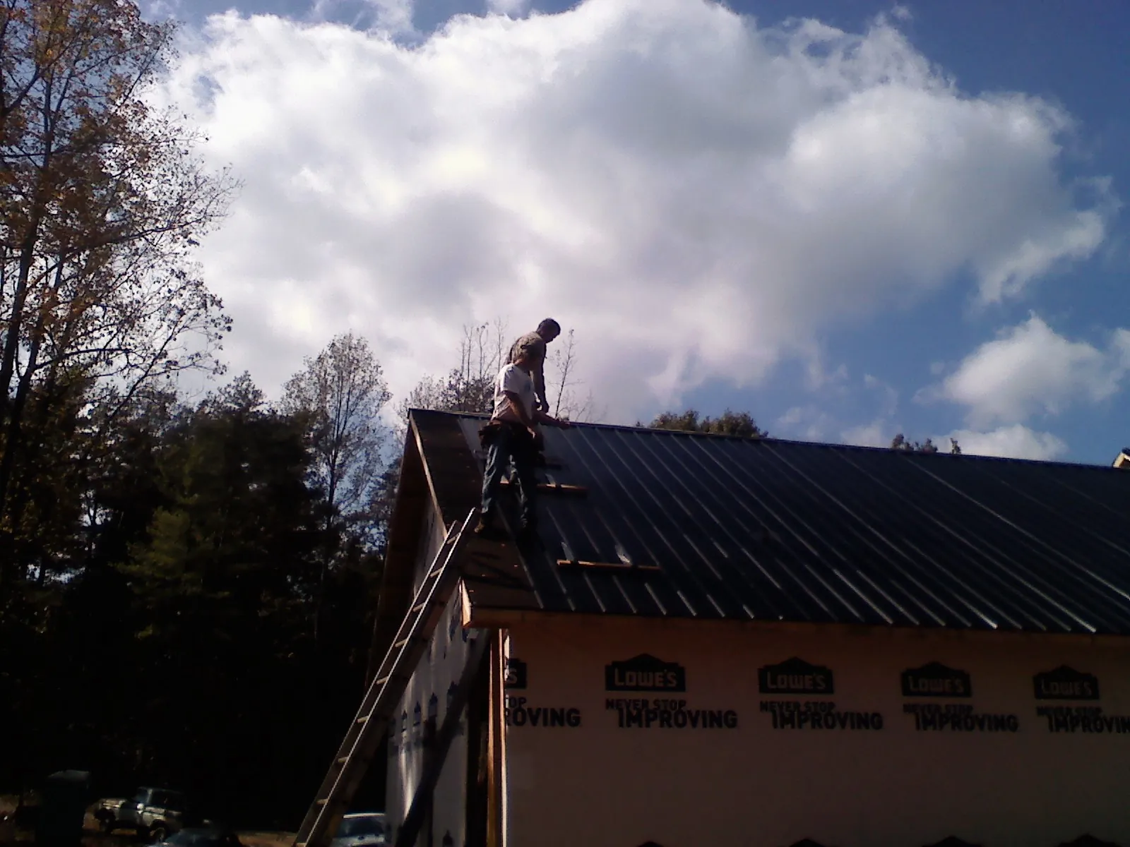 Roofer fastening dark metal panels high against a cloudy sky, from a Roof Inspection job in Rawlings